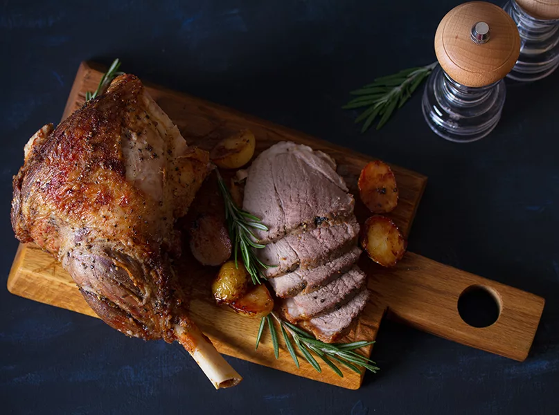 Roast leg of lamb with potatoes and rosemary on dark background