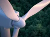 Close up of wind turbine with lush forest in the background.