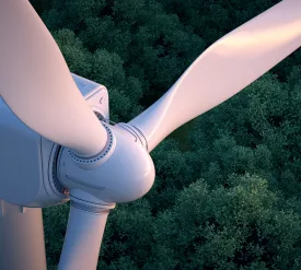 Close up of wind turbine with lush forest in the background.
