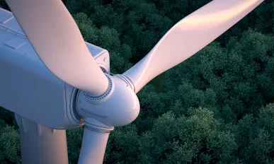 Close up of wind turbine with lush forest in the background.