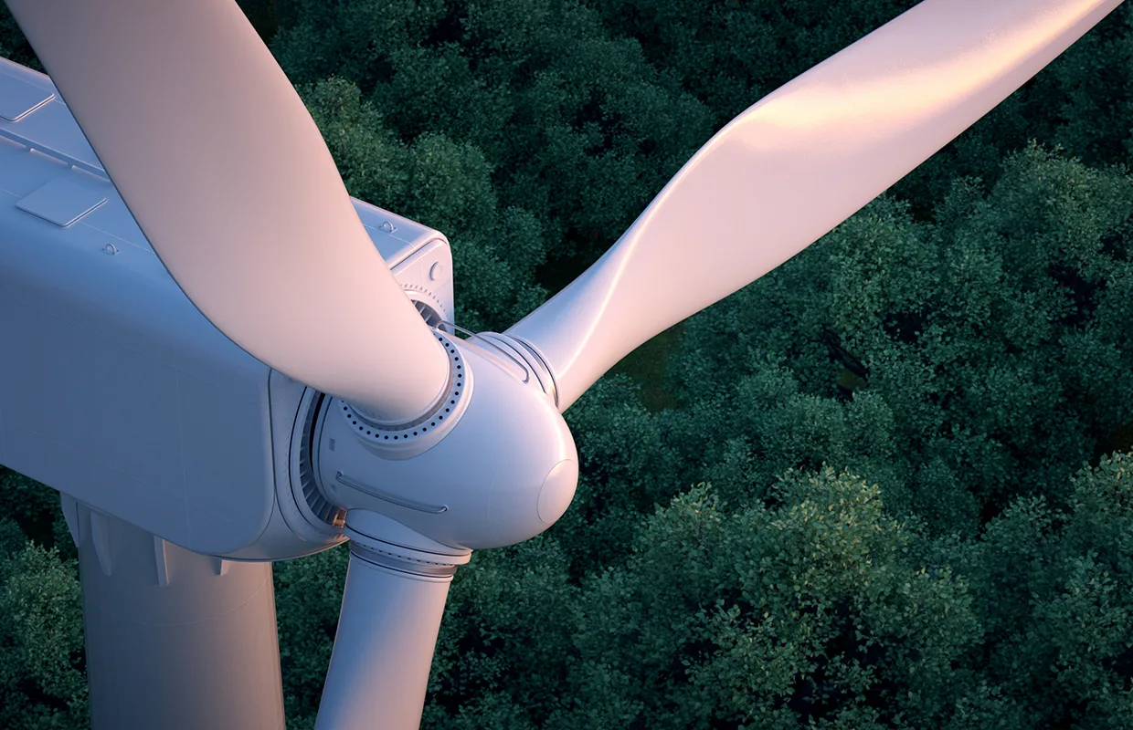 Close up of wind turbine with lush forest in the background.